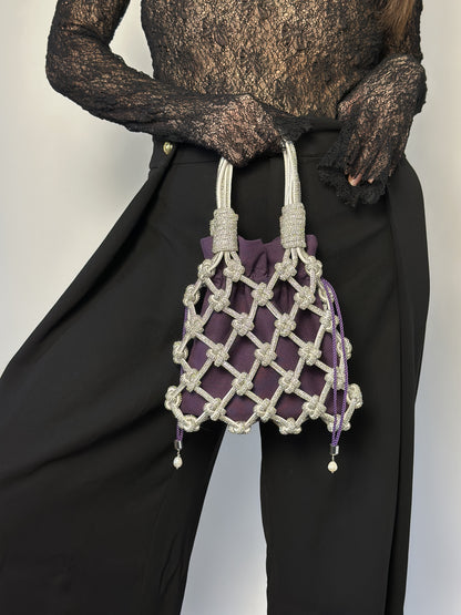 Person holding a purple drawstring bag inside a rhinestone macrame bag against a plain background