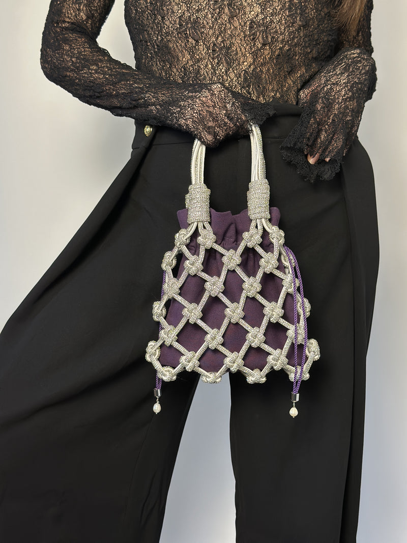 Person holding a purple drawstring bag inside a rhinestone macrame bag against a plain background